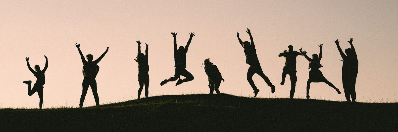 silhouette of many people with arms raised against pink sky